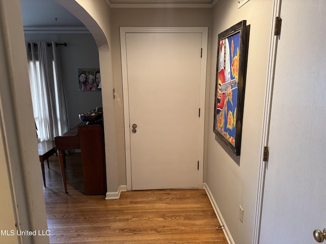 hallway featuring baseboards, arched walkways, wood finished floors, and ornamental molding