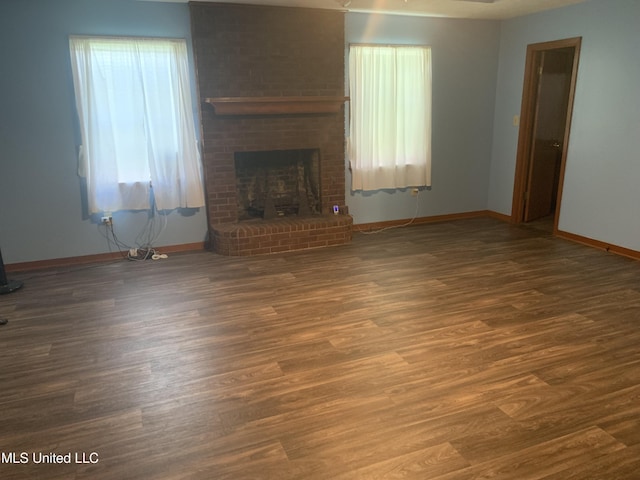 unfurnished living room with a brick fireplace, wood finished floors, and baseboards