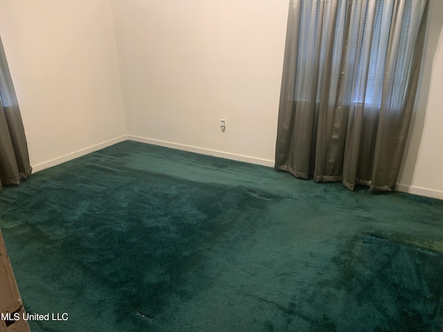 empty room featuring dark colored carpet and baseboards