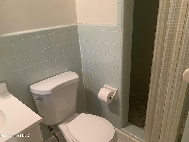 bathroom featuring toilet, a wainscoted wall, a stall shower, and tile walls