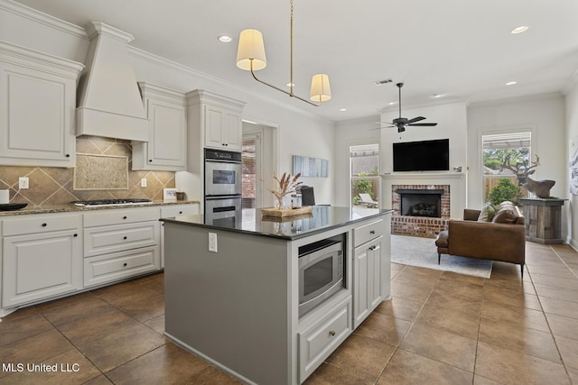 kitchen with appliances with stainless steel finishes, custom exhaust hood, ceiling fan, a fireplace, and a center island
