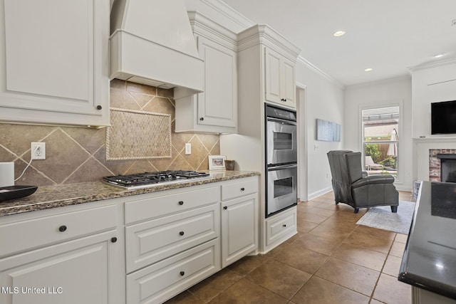 kitchen with custom exhaust hood, stainless steel appliances, ornamental molding, a brick fireplace, and white cabinets