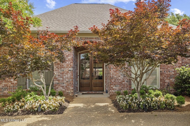view of exterior entry with brick siding, french doors, and a shingled roof