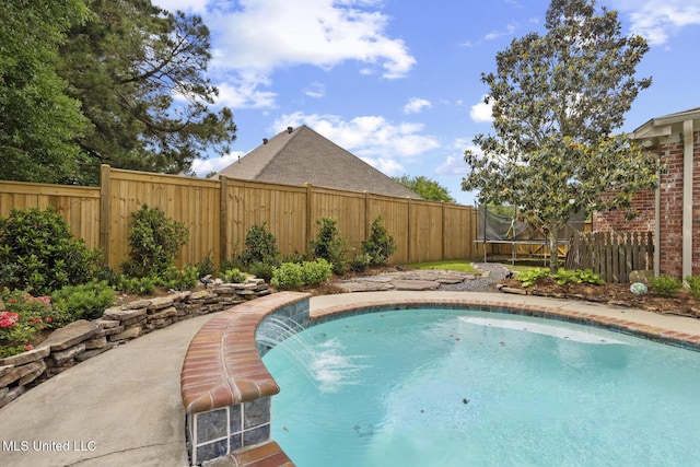 view of swimming pool featuring a trampoline and a fenced backyard