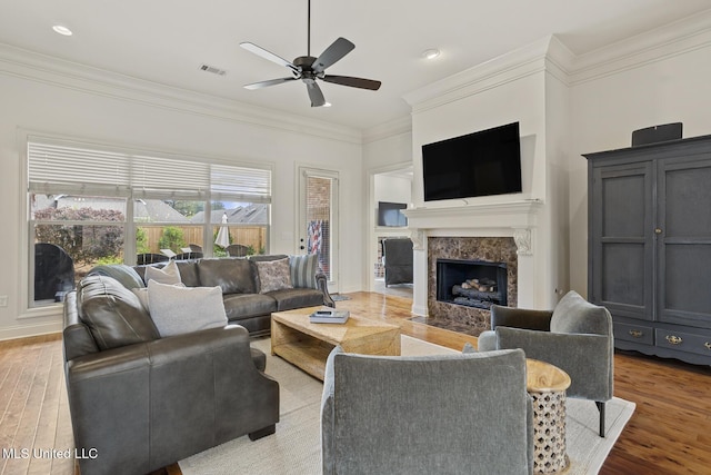 living room featuring a ceiling fan, a fireplace, wood finished floors, crown molding, and baseboards