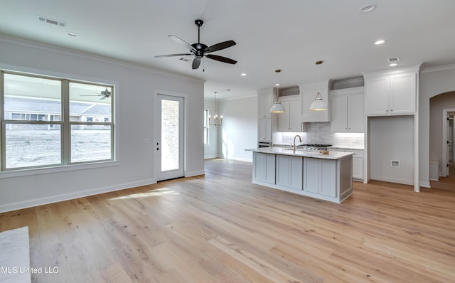 kitchen featuring crown molding, hanging light fixtures, light wood-type flooring, white cabinetry, and an island with sink