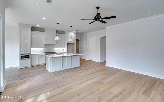 kitchen with hanging light fixtures, sink, white cabinets, a center island with sink, and decorative backsplash