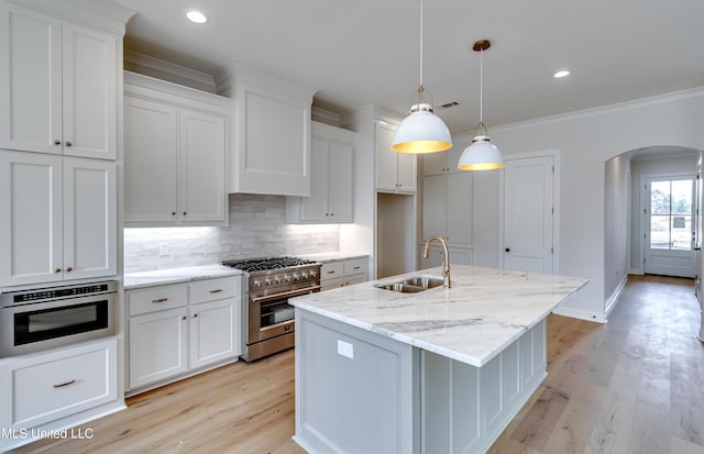 kitchen with stainless steel stove, white cabinetry, hanging light fixtures, a kitchen island with sink, and sink