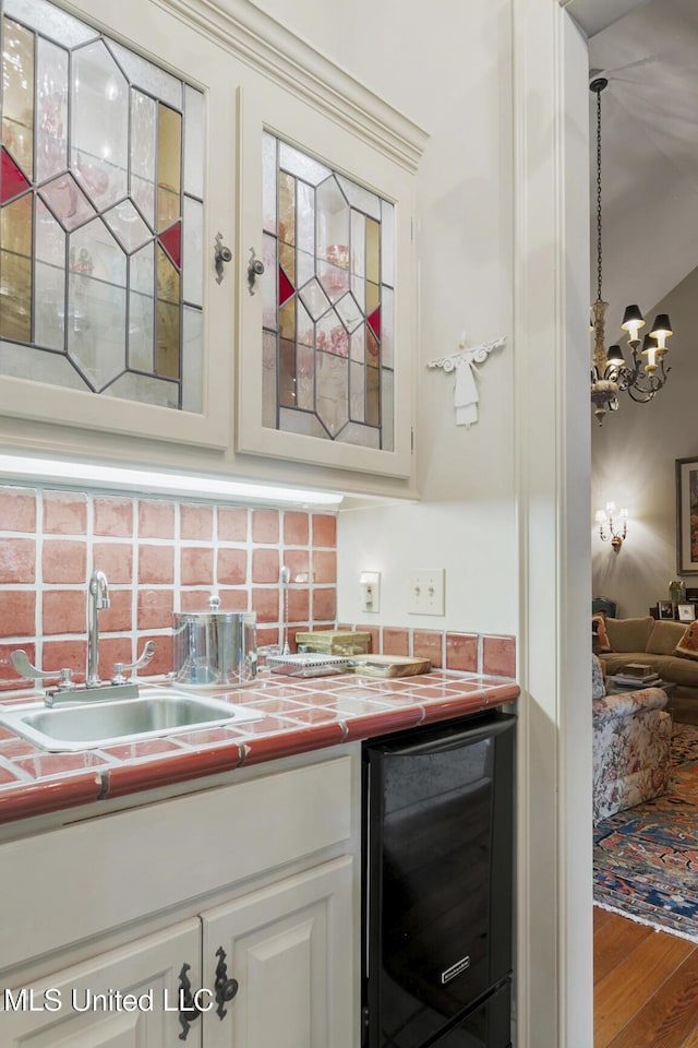 bar with wood-type flooring, sink, an inviting chandelier, white cabinetry, and beverage cooler