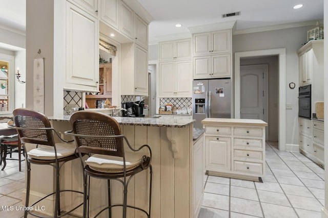 kitchen featuring light stone counters, black oven, stainless steel refrigerator with ice dispenser, and kitchen peninsula