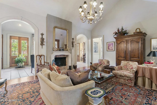 living room with high vaulted ceiling, light hardwood / wood-style flooring, a chandelier, and a fireplace