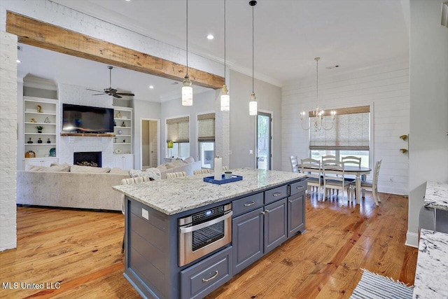 kitchen featuring light wood-style floors, stainless steel oven, a large fireplace, ceiling fan with notable chandelier, and decorative light fixtures