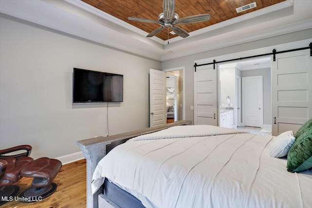 bedroom with visible vents, a barn door, wood finished floors, and a raised ceiling