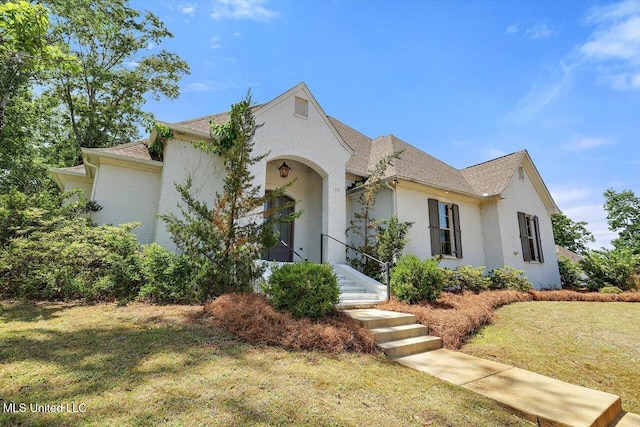 view of front of house featuring a shingled roof, stucco siding, and a front lawn