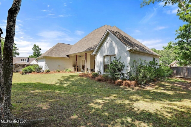 rear view of house featuring fence, stucco siding, a yard, and roof with shingles