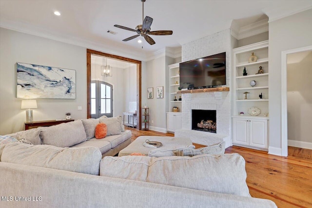 living area featuring a ceiling fan, visible vents, a brick fireplace, light wood-style floors, and ornamental molding