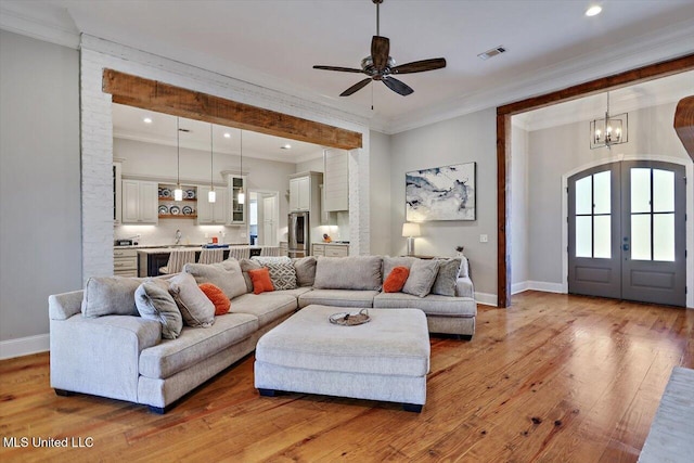 living area featuring crown molding, baseboards, light wood-style flooring, and ceiling fan with notable chandelier