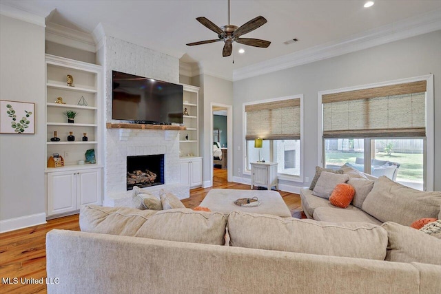 living room with a ceiling fan, visible vents, a brick fireplace, light wood finished floors, and ornamental molding