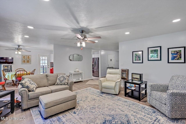 living room featuring light hardwood / wood-style flooring, a textured ceiling, and ceiling fan