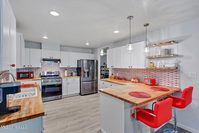 kitchen featuring white cabinetry, butcher block counters, appliances with stainless steel finishes, and decorative light fixtures