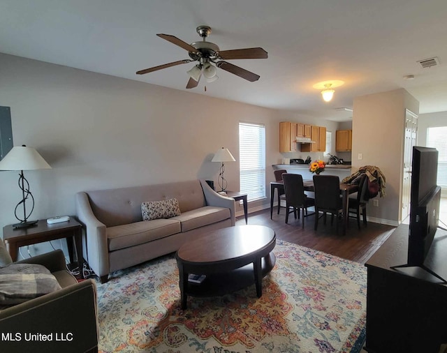 living room featuring ceiling fan, a wealth of natural light, and dark wood-type flooring