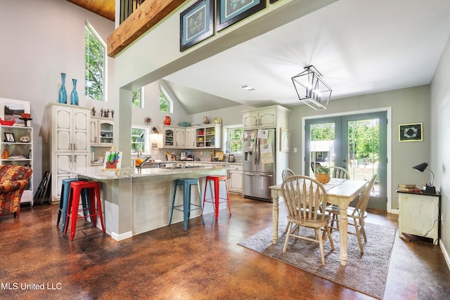 interior space with concrete flooring, light stone countertops, a breakfast bar, stainless steel fridge with ice dispenser, and glass insert cabinets