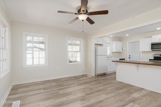 kitchen featuring crown molding, light wood finished floors, appliances with stainless steel finishes, a healthy amount of sunlight, and a kitchen breakfast bar