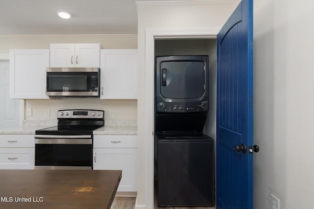 kitchen with white cabinetry, stacked washer / drying machine, light countertops, ornamental molding, and appliances with stainless steel finishes