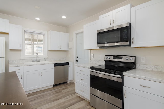 kitchen featuring light wood-style flooring, appliances with stainless steel finishes, crown molding, white cabinetry, and a sink