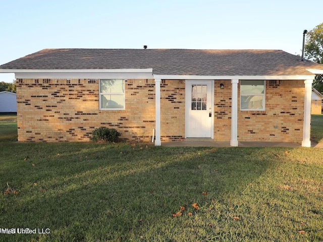 view of front of property with roof with shingles, a front yard, and brick siding