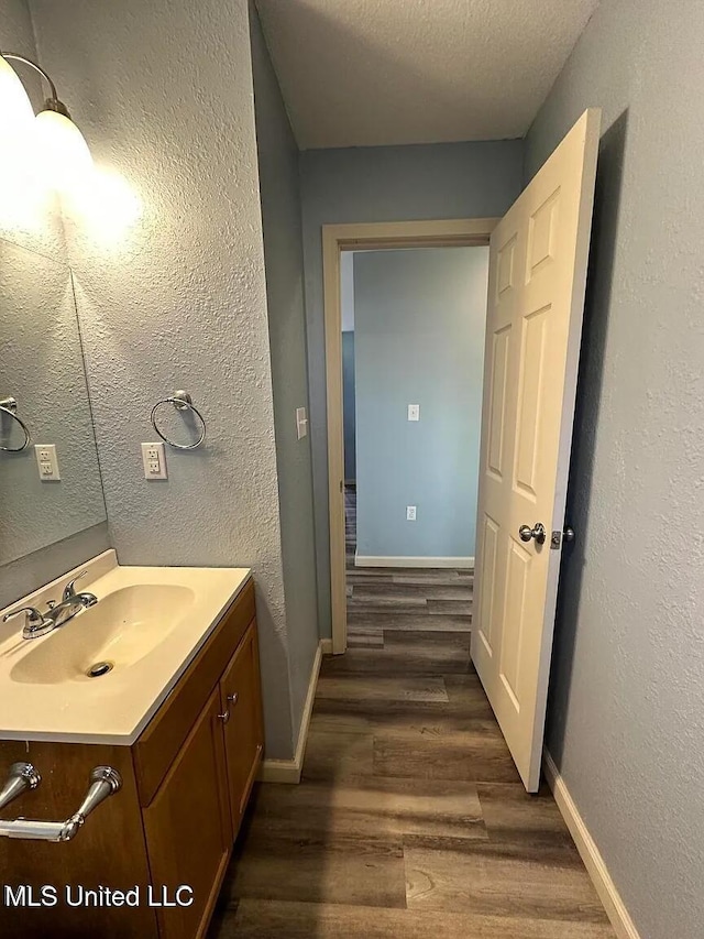 bathroom with a textured ceiling, baseboards, wood finished floors, and vanity