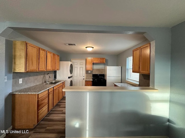 kitchen with black range oven, visible vents, freestanding refrigerator, stacked washer / dryer, and a sink