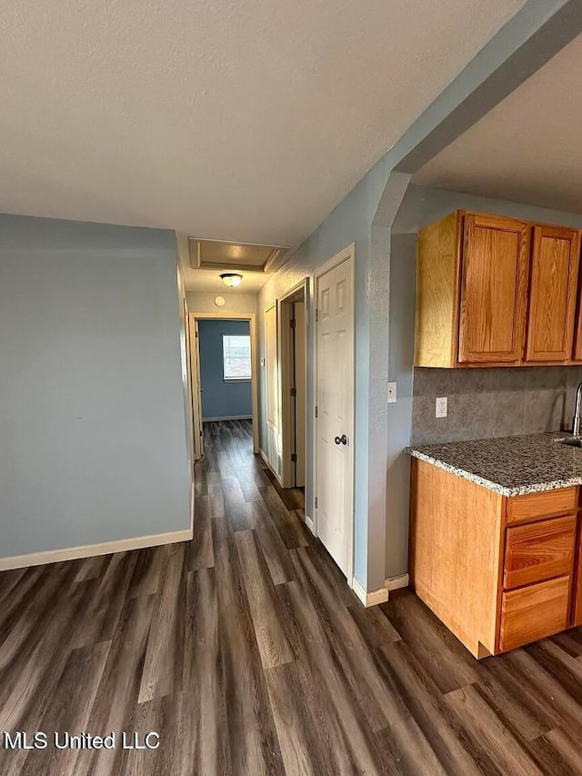 kitchen with baseboards, brown cabinets, dark wood-type flooring, stone counters, and backsplash