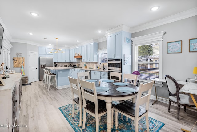 dining space with crown molding, sink, a chandelier, and light wood-type flooring