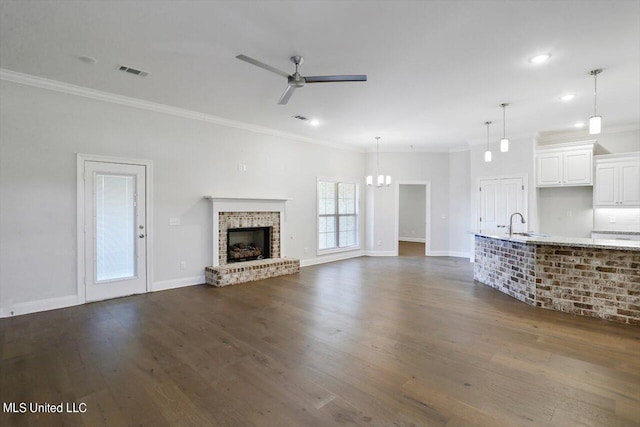 unfurnished living room featuring dark wood-type flooring, a fireplace, crown molding, and ceiling fan with notable chandelier