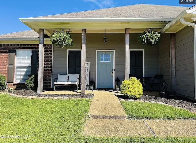 view of exterior entry featuring covered porch and a lawn