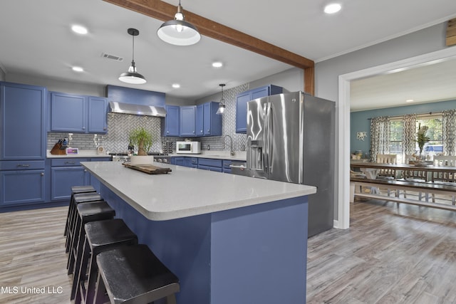 56 53rd St, Gulfport, MS 39507 - kitchen featuring blue cabinetry, white microwave, wall chimney exhaust hood, stainless steel fridge, and a kitchen breakfast bar