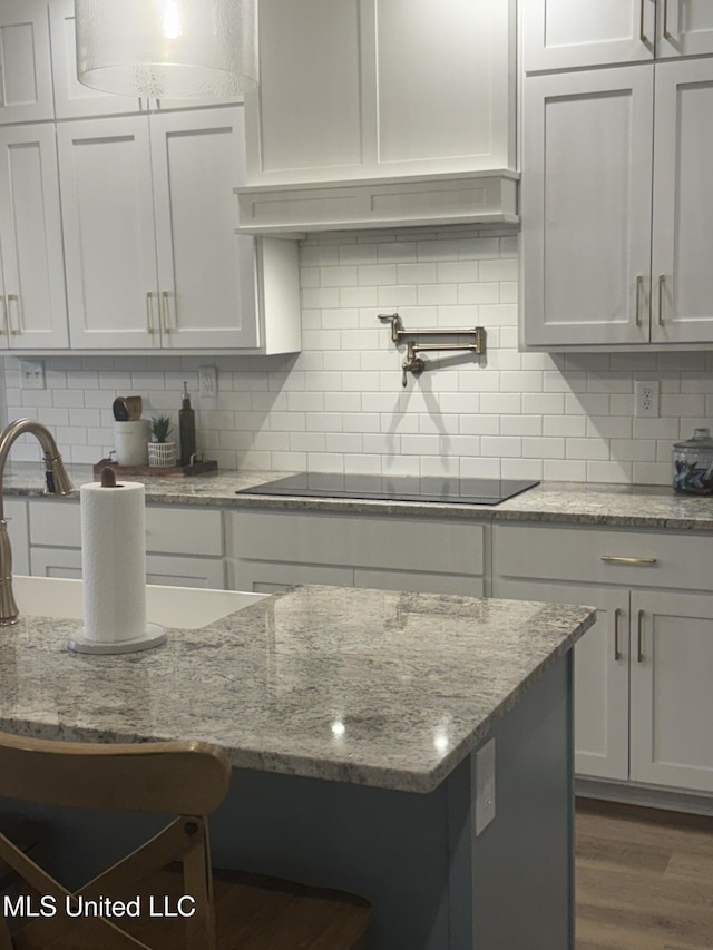 kitchen featuring tasteful backsplash, dark wood-style flooring, light stone counters, and black electric cooktop