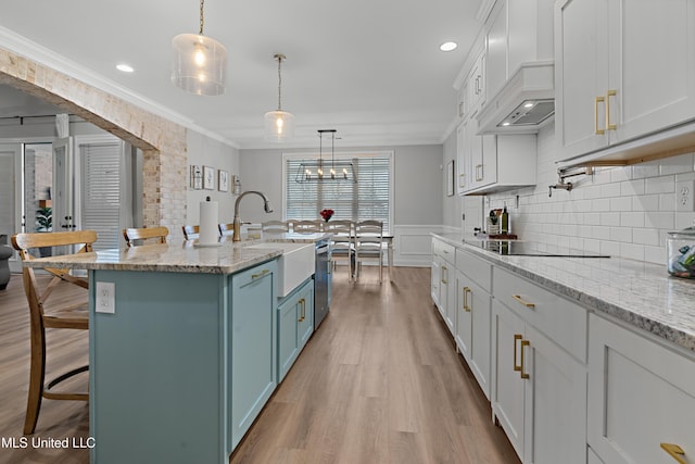 kitchen featuring a breakfast bar, custom exhaust hood, light wood-style flooring, ornamental molding, and a sink