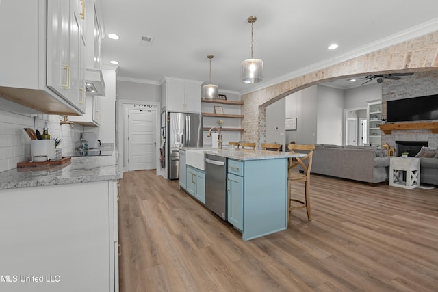 kitchen with arched walkways, blue cabinets, open floor plan, appliances with stainless steel finishes, and crown molding