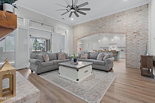 living area with light wood finished floors, ceiling fan, arched walkways, and ornamental molding