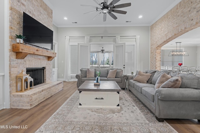 living room featuring wood finished floors, visible vents, crown molding, and ceiling fan with notable chandelier