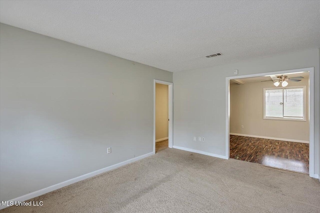 spare room with carpet floors, visible vents, a ceiling fan, a textured ceiling, and baseboards