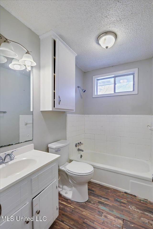 bathroom with toilet, a tub, wood finished floors, a textured ceiling, and vanity