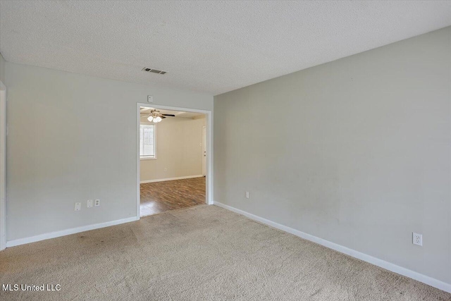 spare room with carpet floors, visible vents, a textured ceiling, and baseboards