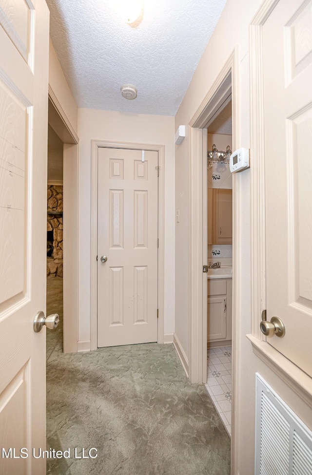 corridor with light carpet and a textured ceiling