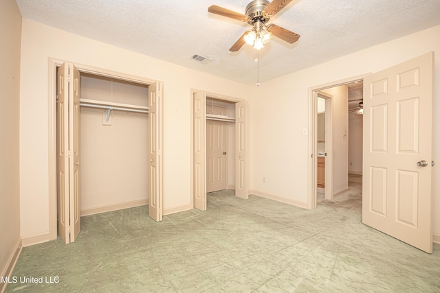 unfurnished bedroom with a textured ceiling, two closets, and ceiling fan