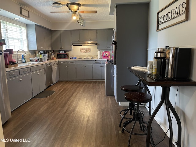 kitchen featuring stainless steel dishwasher, under cabinet range hood, a sink, gray cabinetry, and dark wood-type flooring