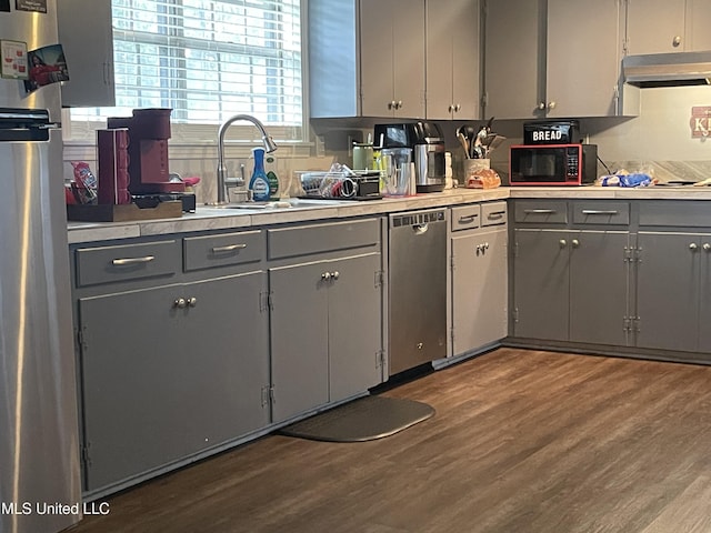 kitchen featuring appliances with stainless steel finishes, dark wood-style flooring, gray cabinetry, and under cabinet range hood