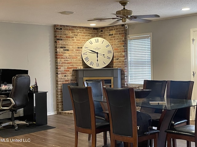 dining room with a textured ceiling, wood finished floors, a ceiling fan, and a brick fireplace
